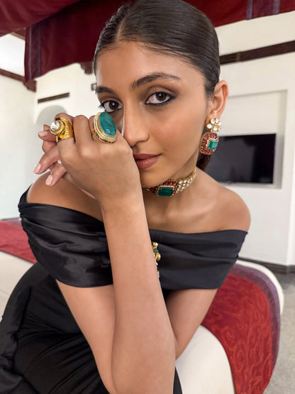 Elegant hands wearing intricate gold cuffs and gemstone rings placed on a retro leather seat
