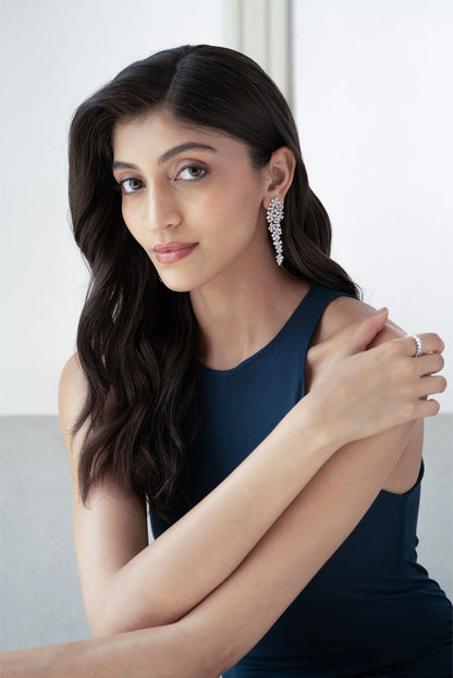 Portrait of a woman wearing a deep blue sleeveless top and long cascading diamond earrings, styled in an elegant, minimal setting.
