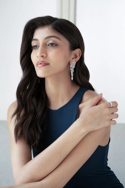 Elegant portrait featuring a woman with wavy hair wearing elongated diamond earrings that form a floral cascade design.
