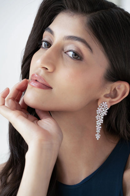 Fine jewelry styling image highlighting sparkling chandelier-style diamond earrings on a woman in a modern blue dress.
