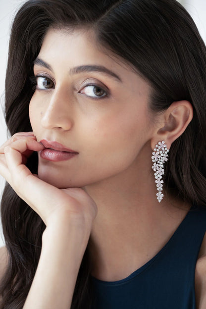 Sophisticated fashion portrait of a woman wearing long diamond earrings with intricate clustered stones against a clean background.
