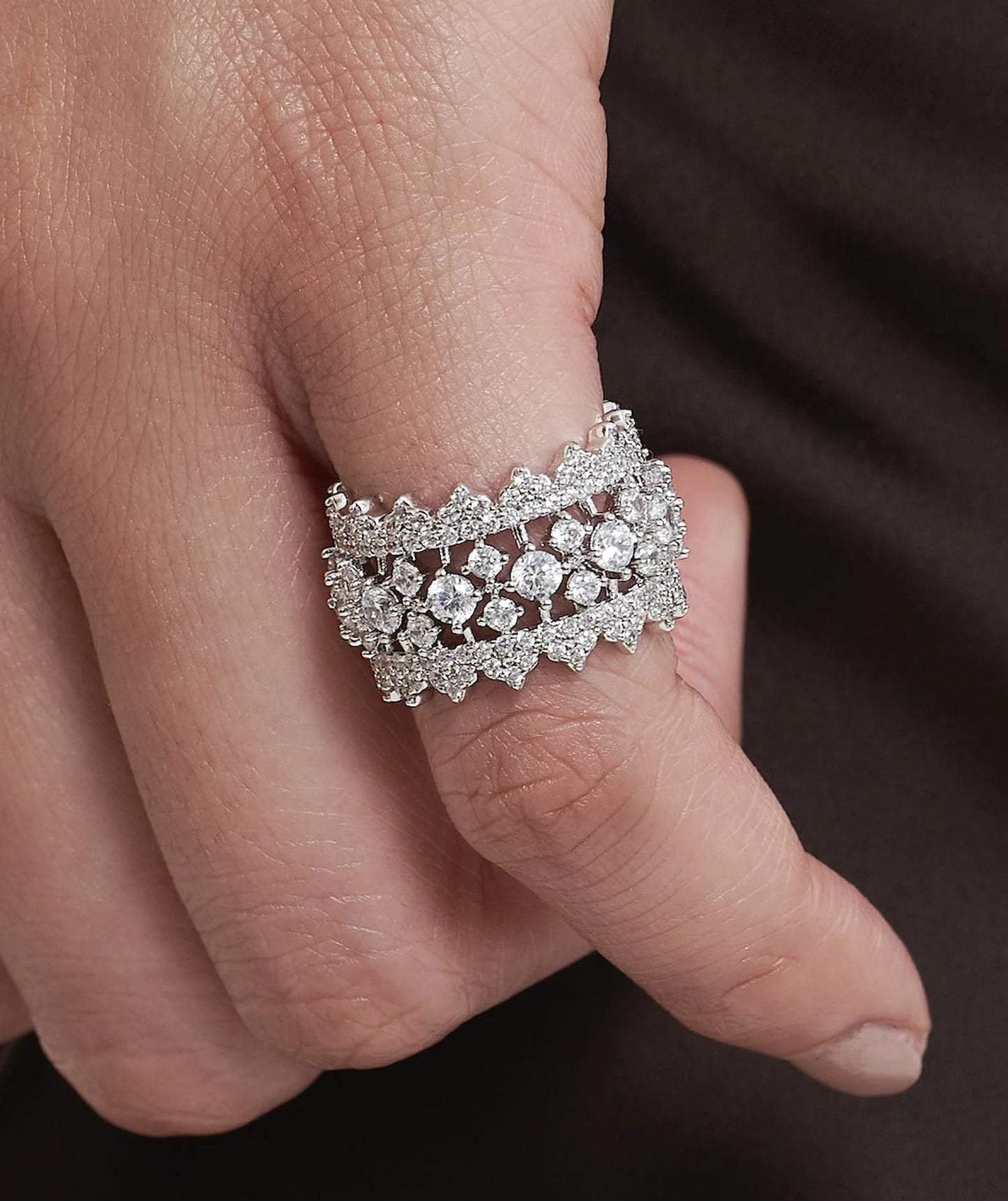 Elegant hand adorned with layered diamond bands and a delicate tennis bracelet, set against a rich, dark garment.
