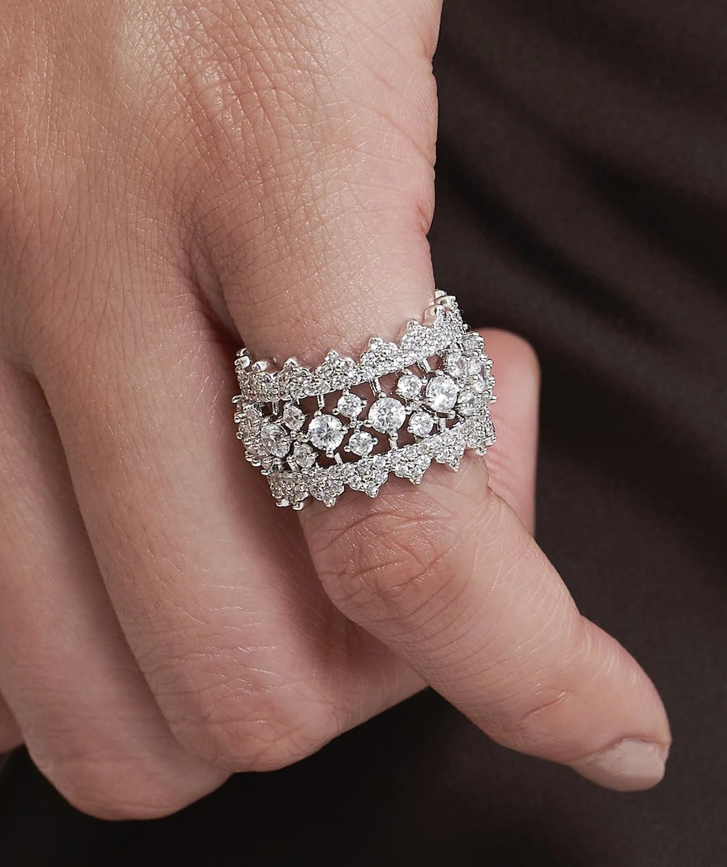 Elegant hand adorned with layered diamond bands and a delicate tennis bracelet, set against a rich, dark garment.
