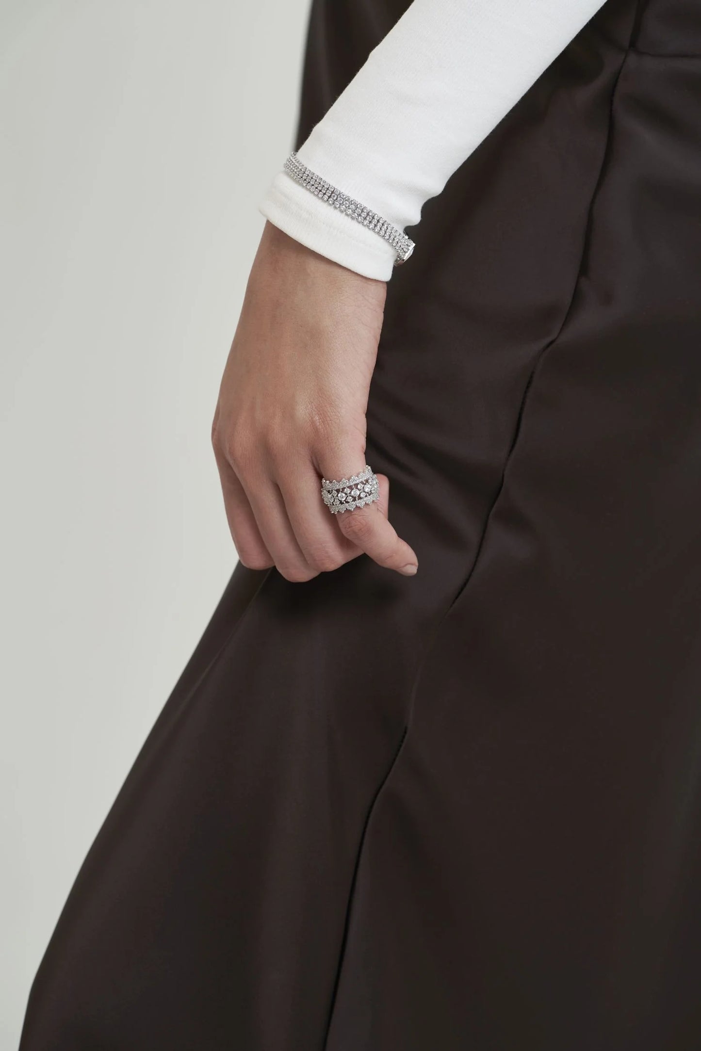 Fine jewelry styling featuring multiple diamond rings and a sparkling bracelet on a hand resting beside deep-toned fabric.
