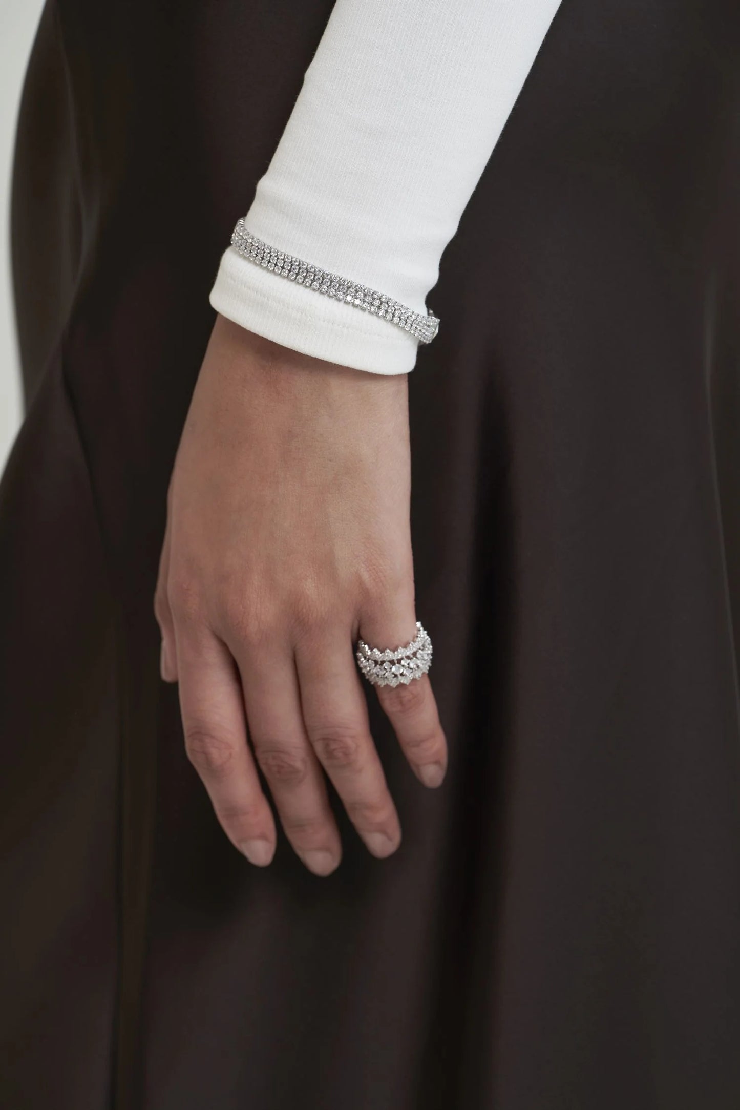 Close-up of a hand showcasing stacked pavé diamond rings and a refined bracelet, paired with a minimalist white sleeve.
