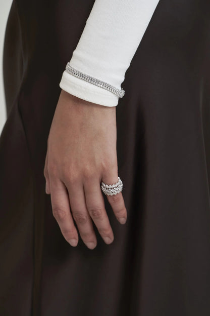 Close-up of a hand showcasing stacked pavé diamond rings and a refined bracelet, paired with a minimalist white sleeve.
