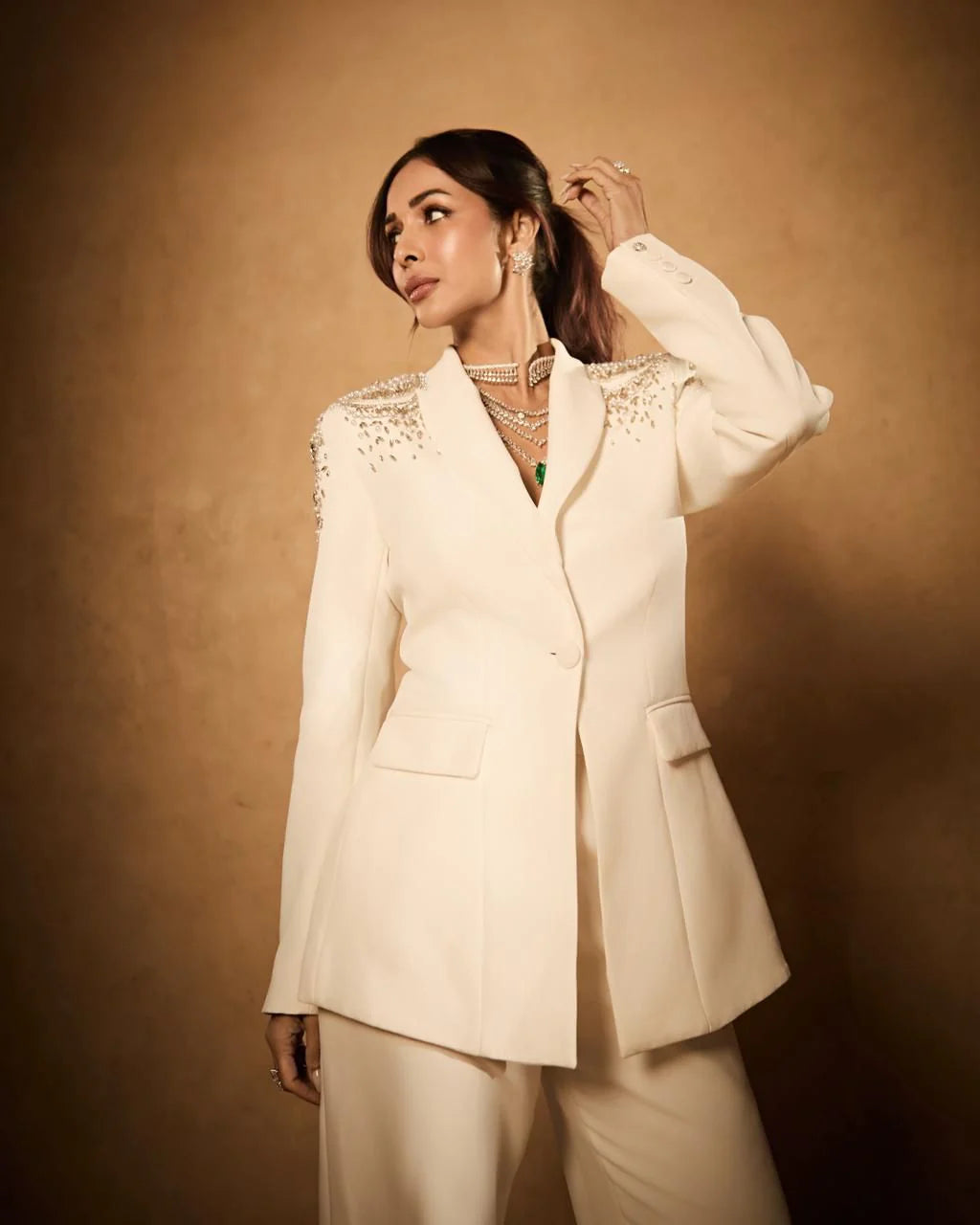 Luxury portrait of woman in cream suit adorned with sparkling shoulder details and layered necklaces
