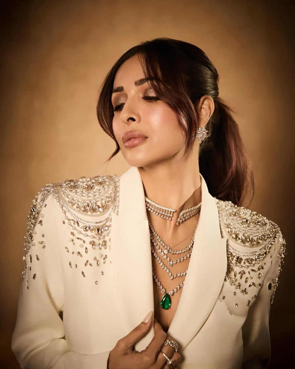 Stylish woman posing in beige blazer with diamond choker and green pendant jewelry
