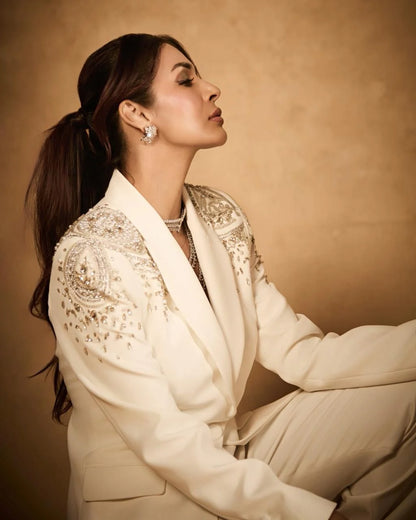 Woman in elegant ivory blazer showcasing luxury diamond jewelry set with emerald centerpiece
