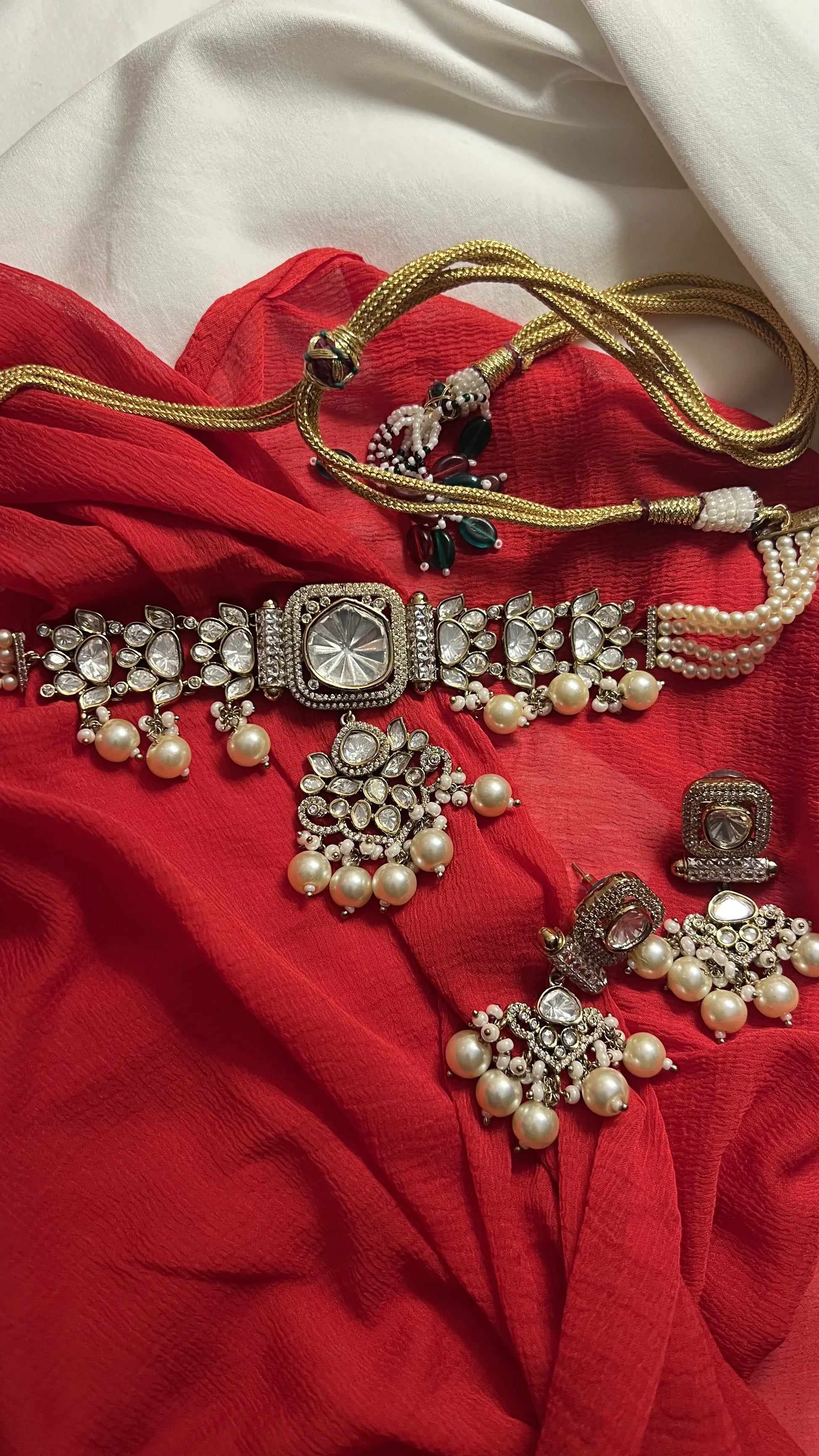 Lifestyle image of a woman seated in a garden wearing a vibrant red lehenga and coordinated jewelry in a natural setting.
