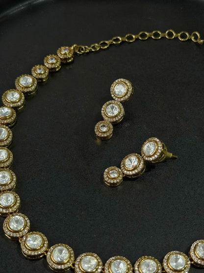 Luxury gold necklace and drop earrings set with round crystal stones on black background
