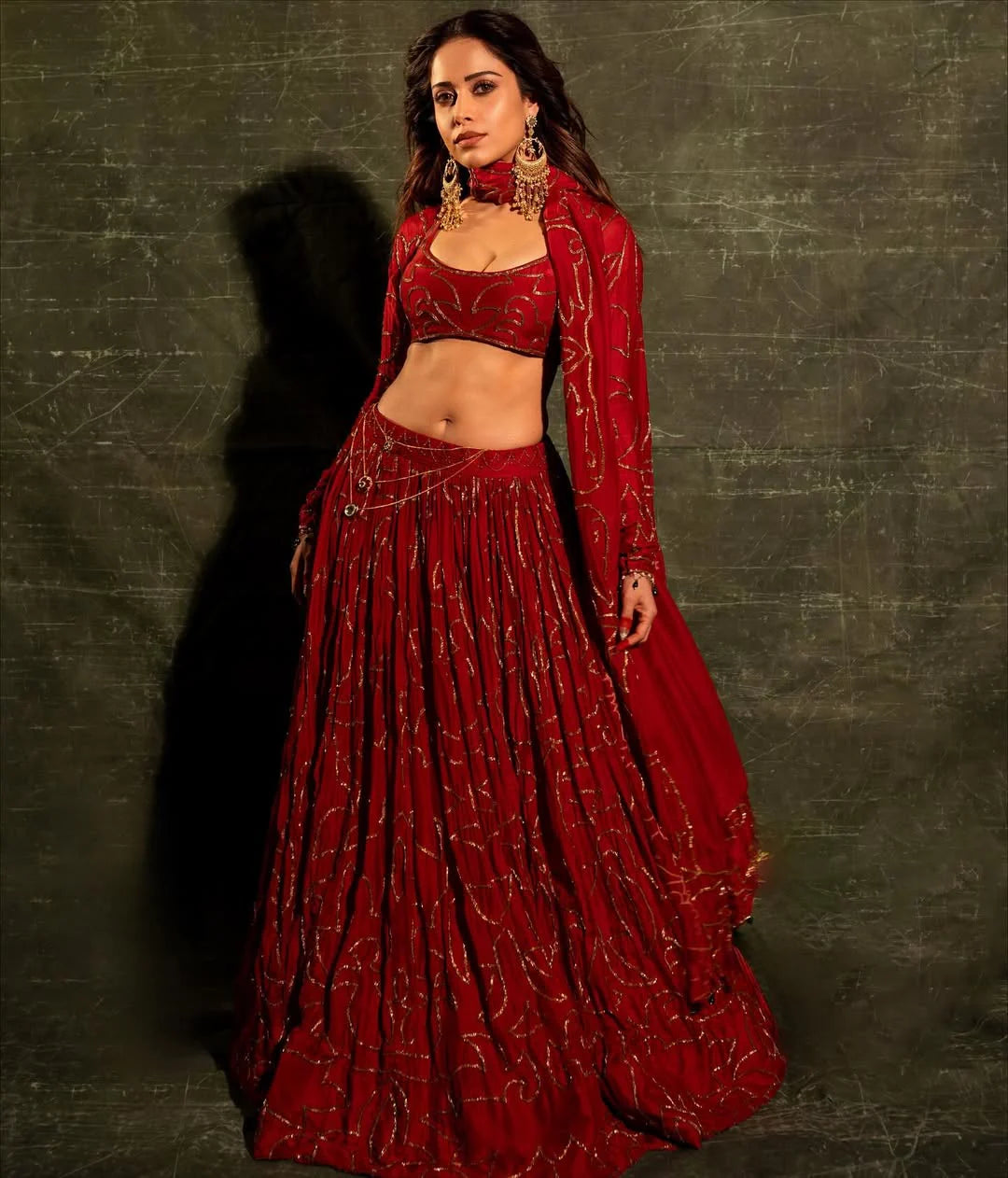 Woman in red festive attire with gold jewelry set and embroidered skirt
