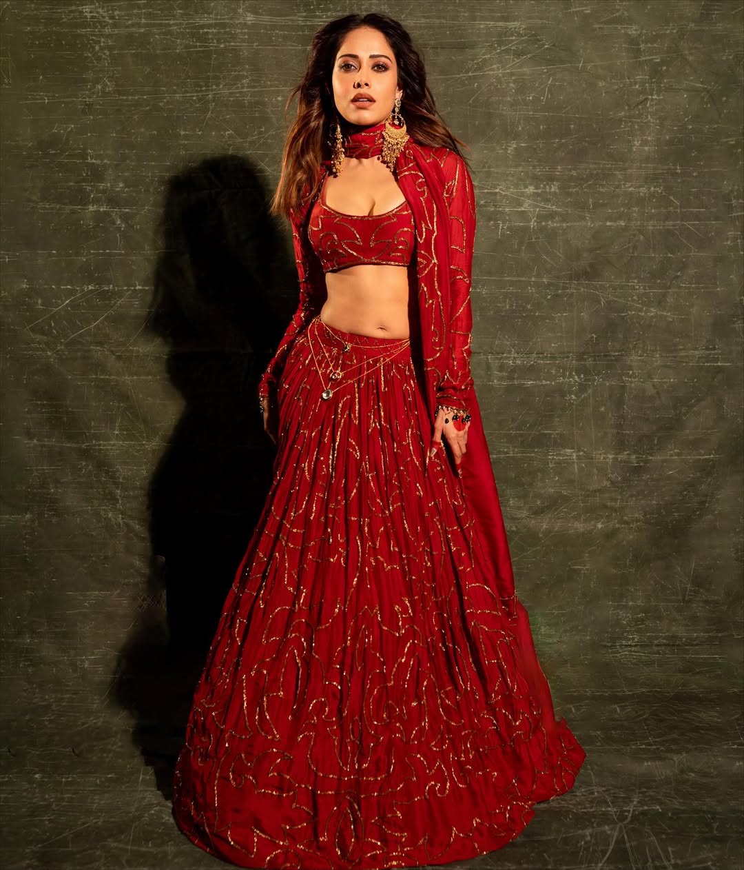 Elegant model wearing red traditional outfit with heavy gold earrings and matching accessories
