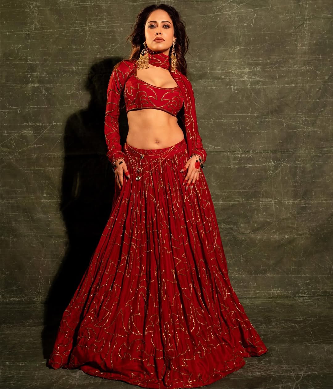 Fashion portrait of woman in red lehenga with intricate gold detailing and bold styling
