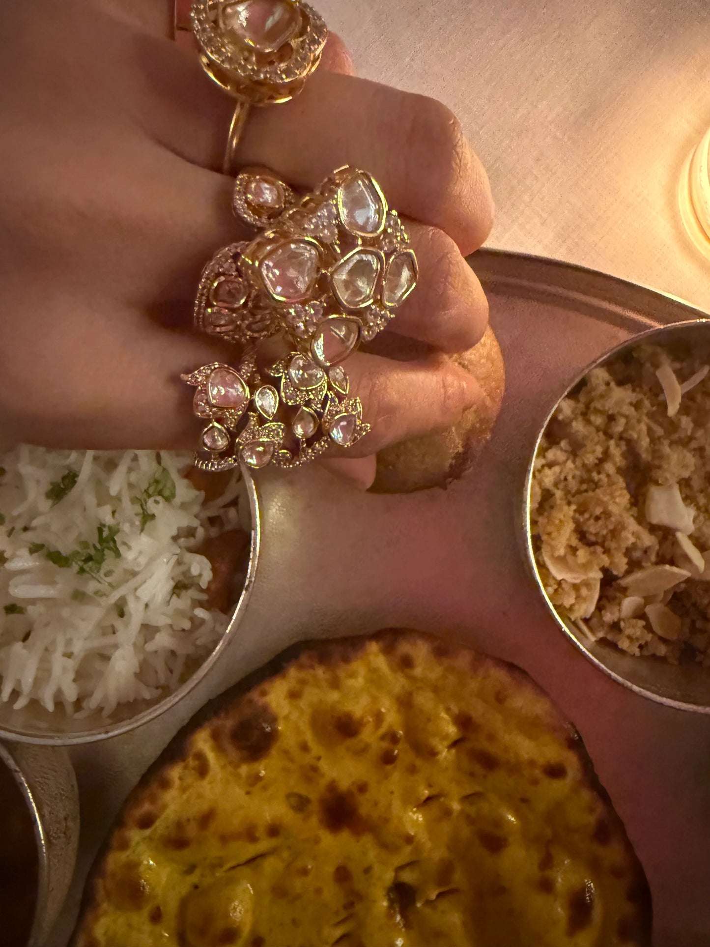 Premium gold rings with intricate designs and clear stones worn on hand over food setting
