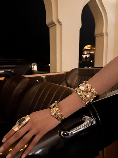 High-end fashion shot of gold bracelets and rings styled on a hand against a vintage automotive backdrop
