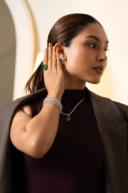 Woman showcasing emerald pendant necklace with diamond chain, paired with matching bracelet and green gemstone ring