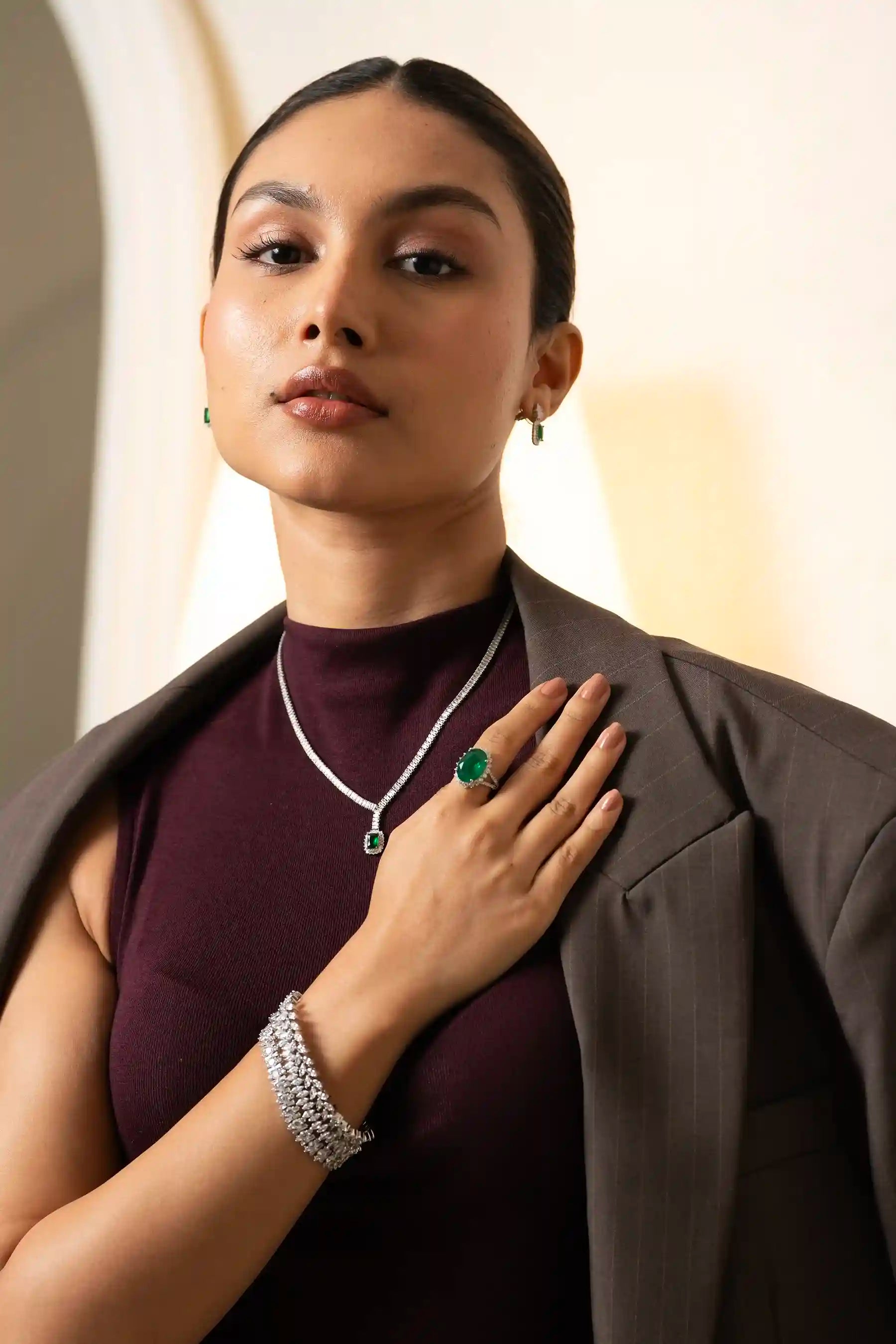 Close-up of model wearing emerald necklace and oval green gemstone ring with diamond accents in luxury jewelry styling