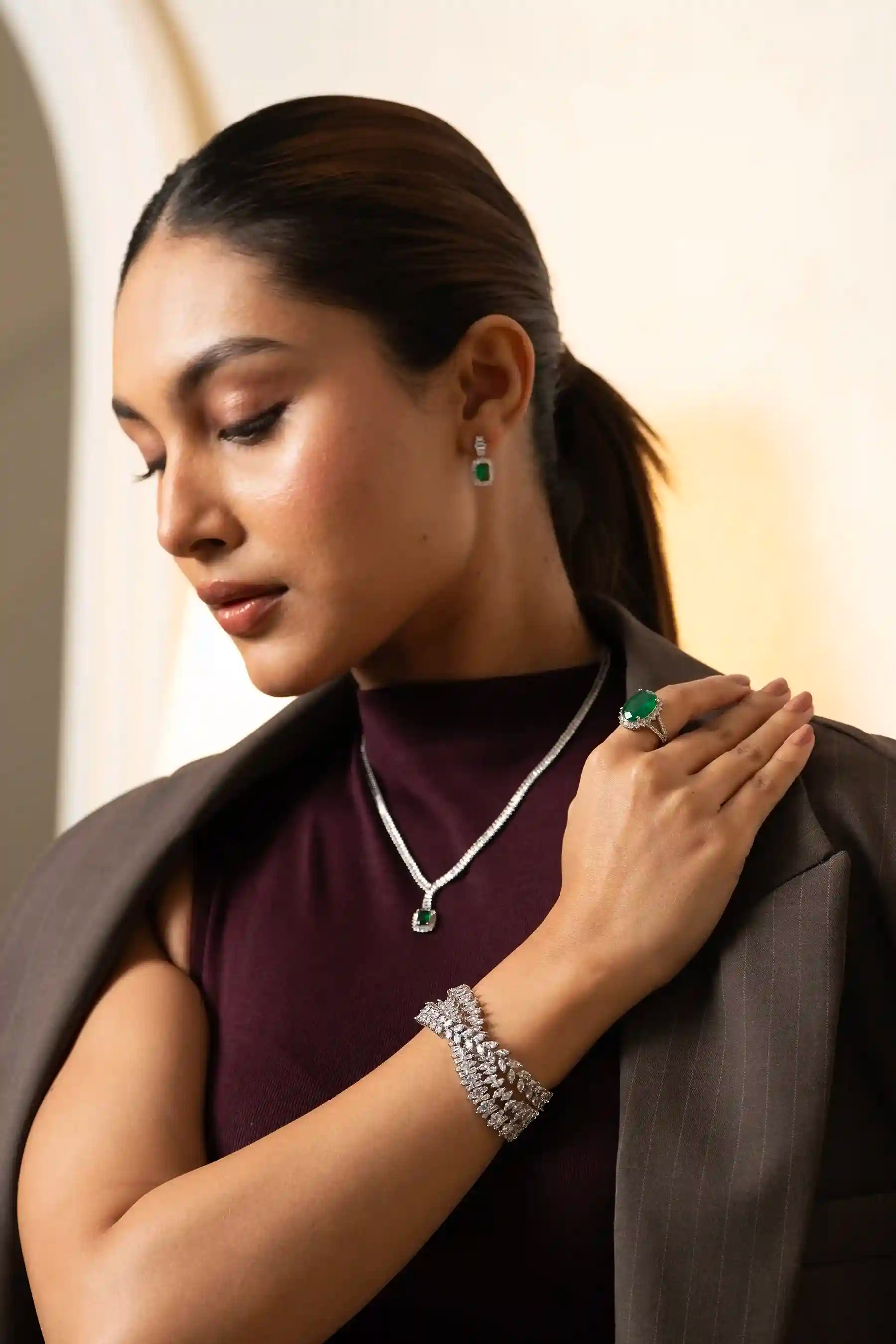 Side profile of model featuring emerald pendant necklace, matching earrings and statement ring in sophisticated fashion look