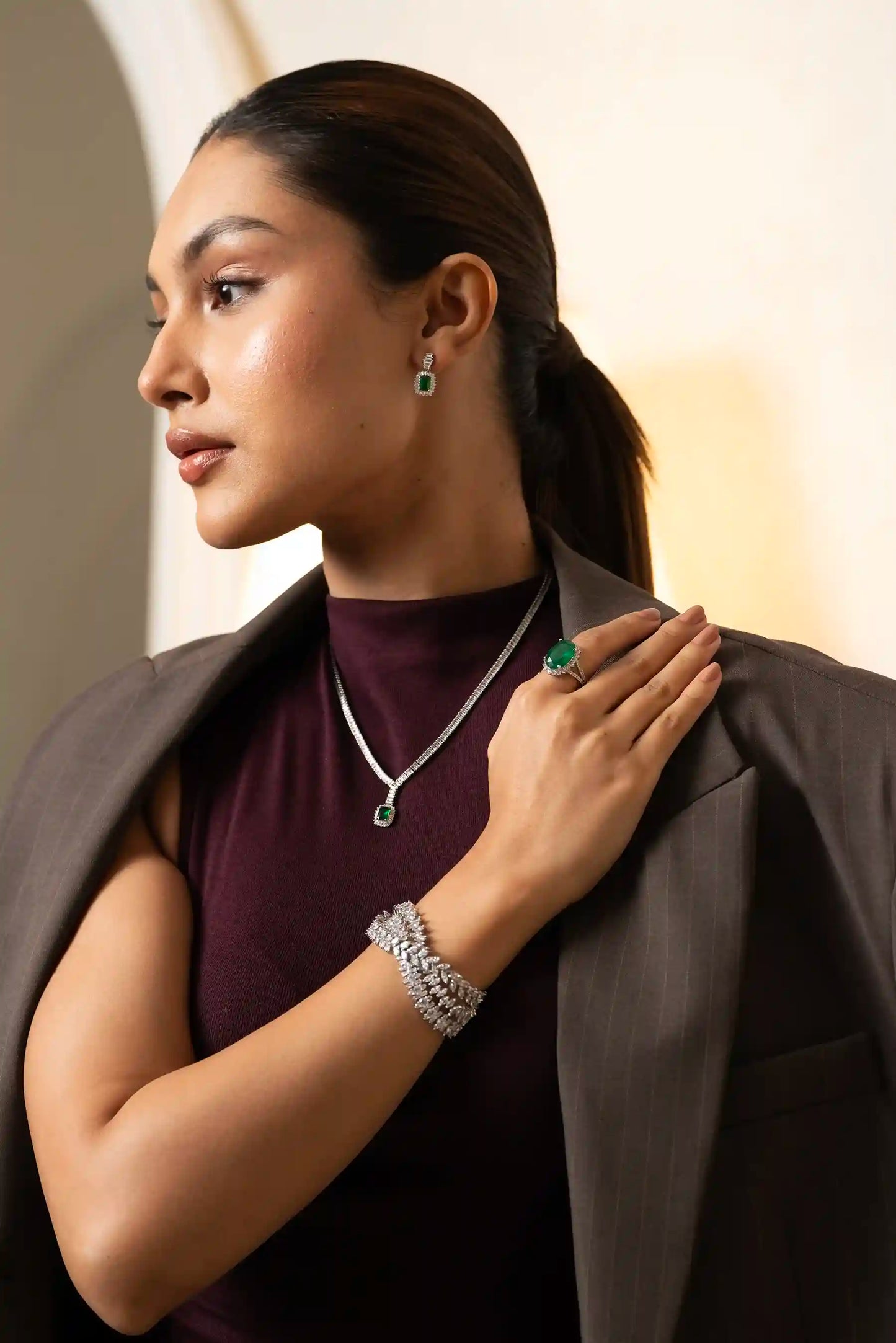Model wearing emerald and diamond jewelry set including necklace, bracelet and ring styled with formal outfit