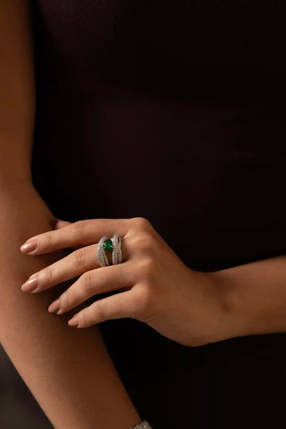 Close-up of emerald and diamond ring with oval green gemstone and layered pavé bands on hand