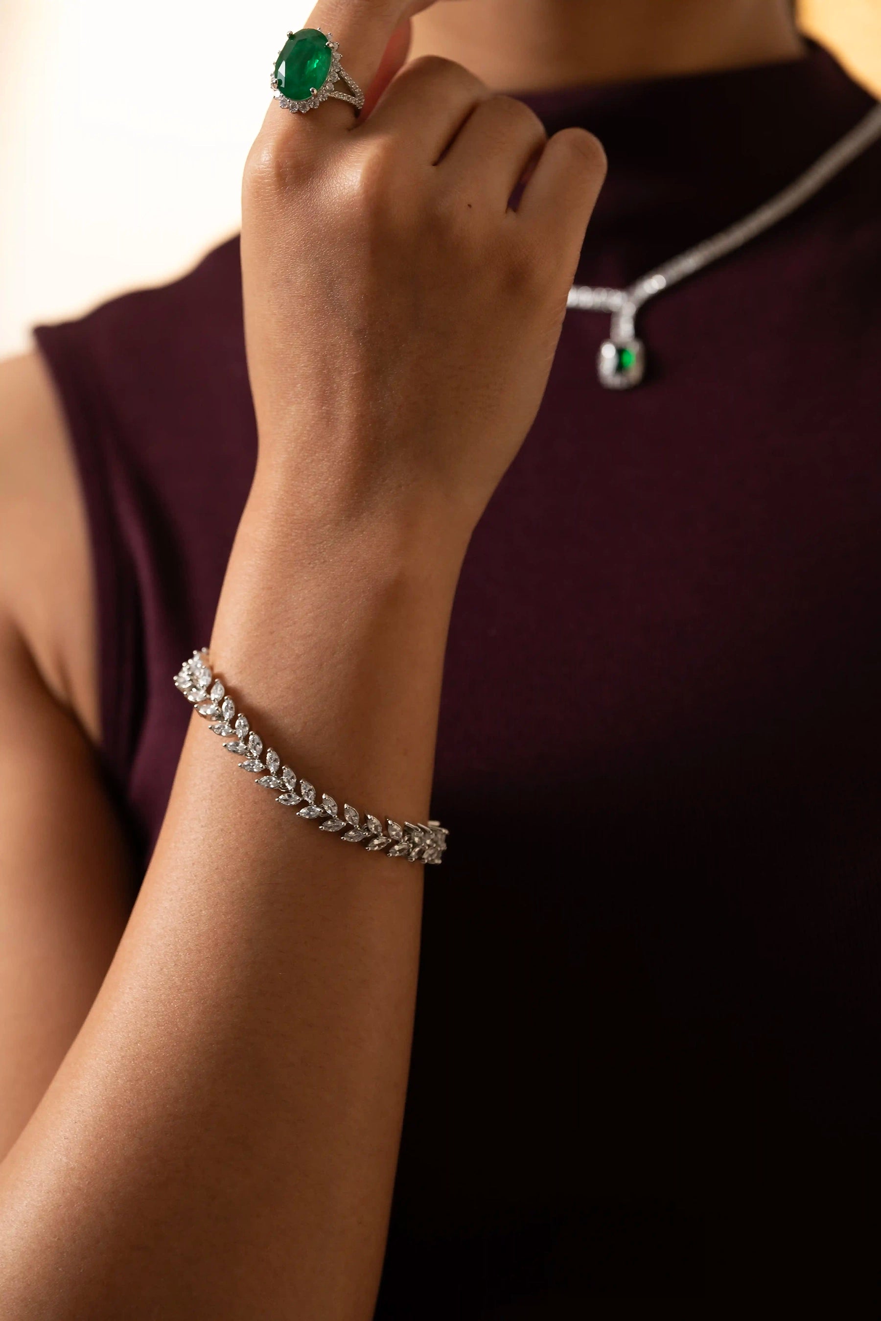 Model wearing diamond tennis bracelet with marquise-cut stones, paired with oval emerald ring and pendant necklace