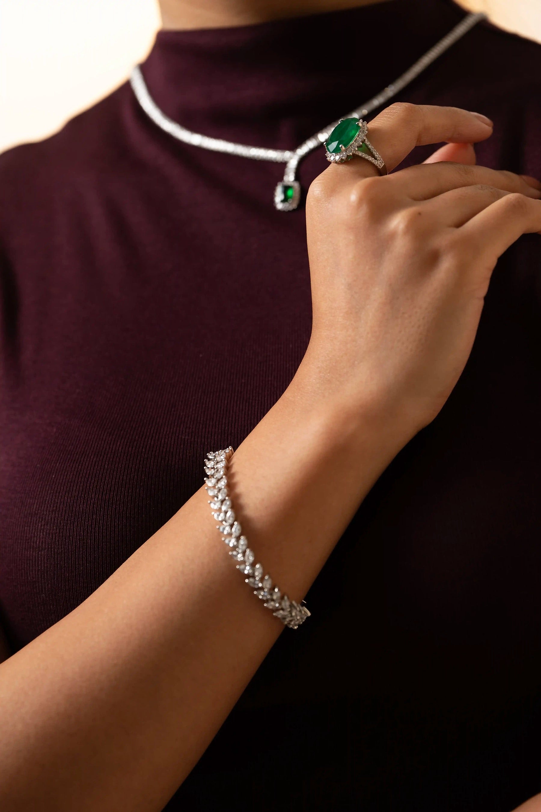 Elegant diamond bracelet with marquise links worn on wrist, styled with oval emerald ring in luxury jewelry look