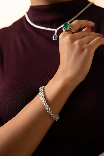 Elegant diamond bracelet with marquise links worn on wrist, styled with oval emerald ring in luxury jewelry look