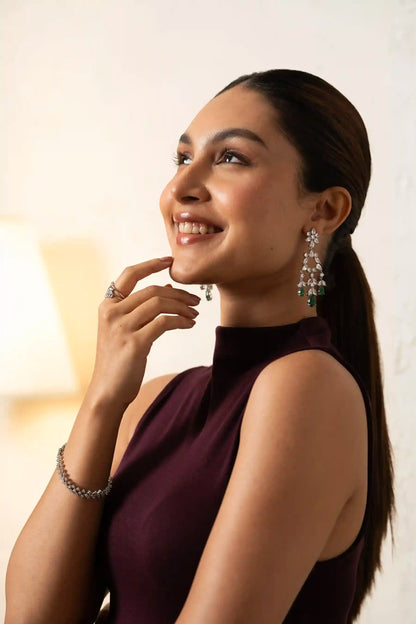 Profile view of woman wearing chandelier diamond earrings with green gemstone accents, luxury jewelry look