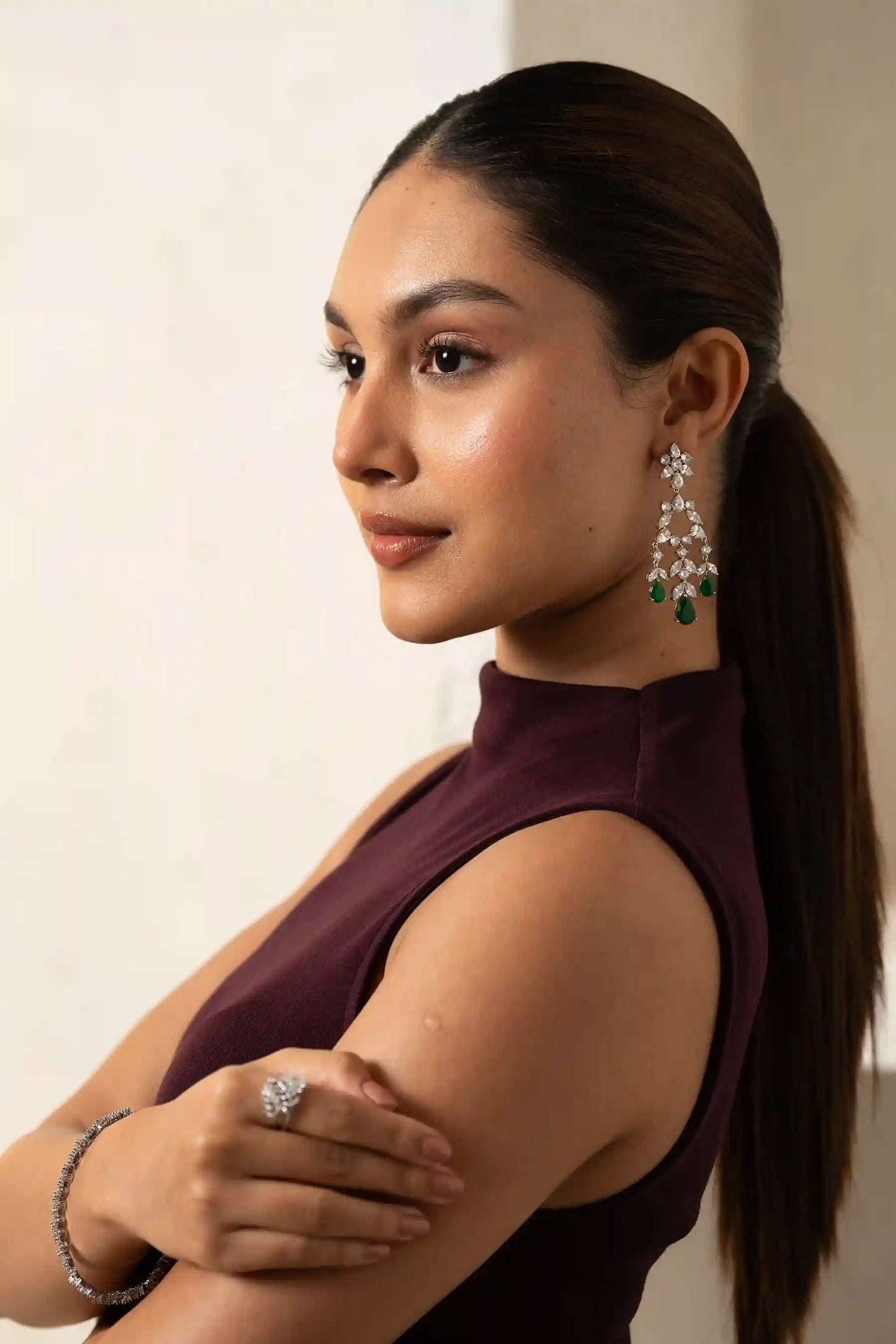Angled portrait of model smiling with diamond and emerald earrings, paired with bracelet and ring