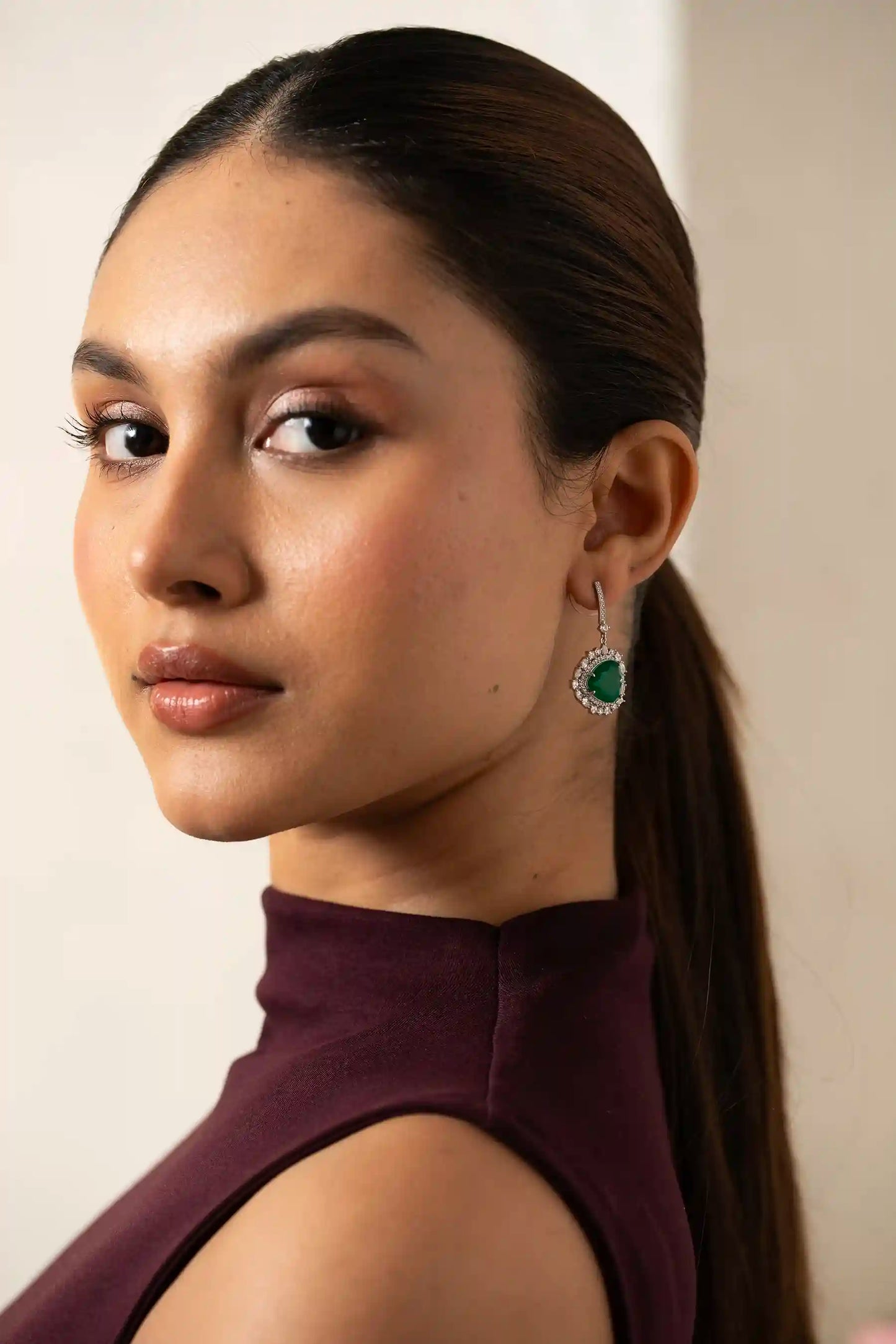 Detailed close-up of a heart-shaped emerald dangle earring with a diamond halo and pavé-set bar on ear.