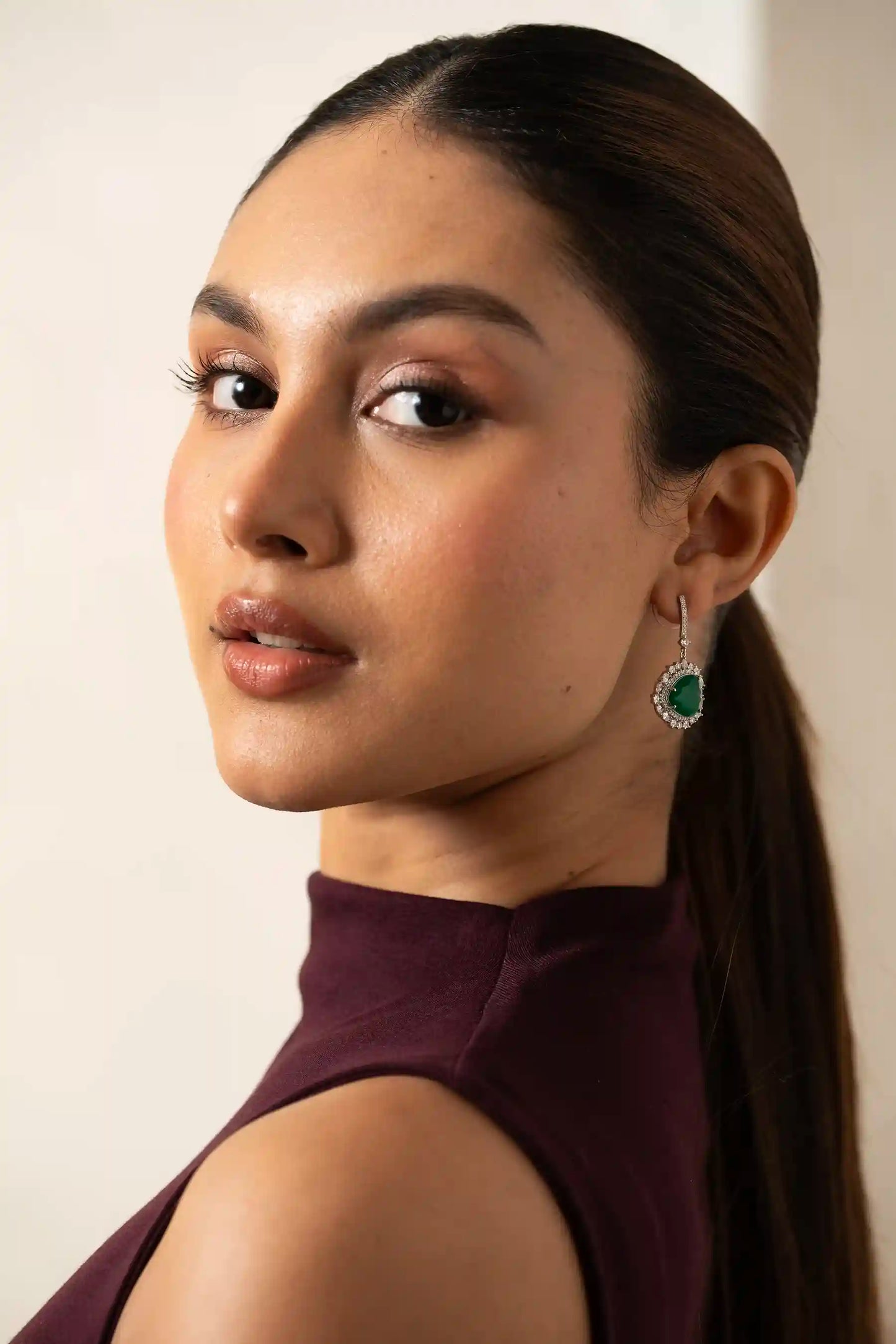 Angled macro shot of a green emerald heart earring framed by brilliant diamonds in a halo drop design.