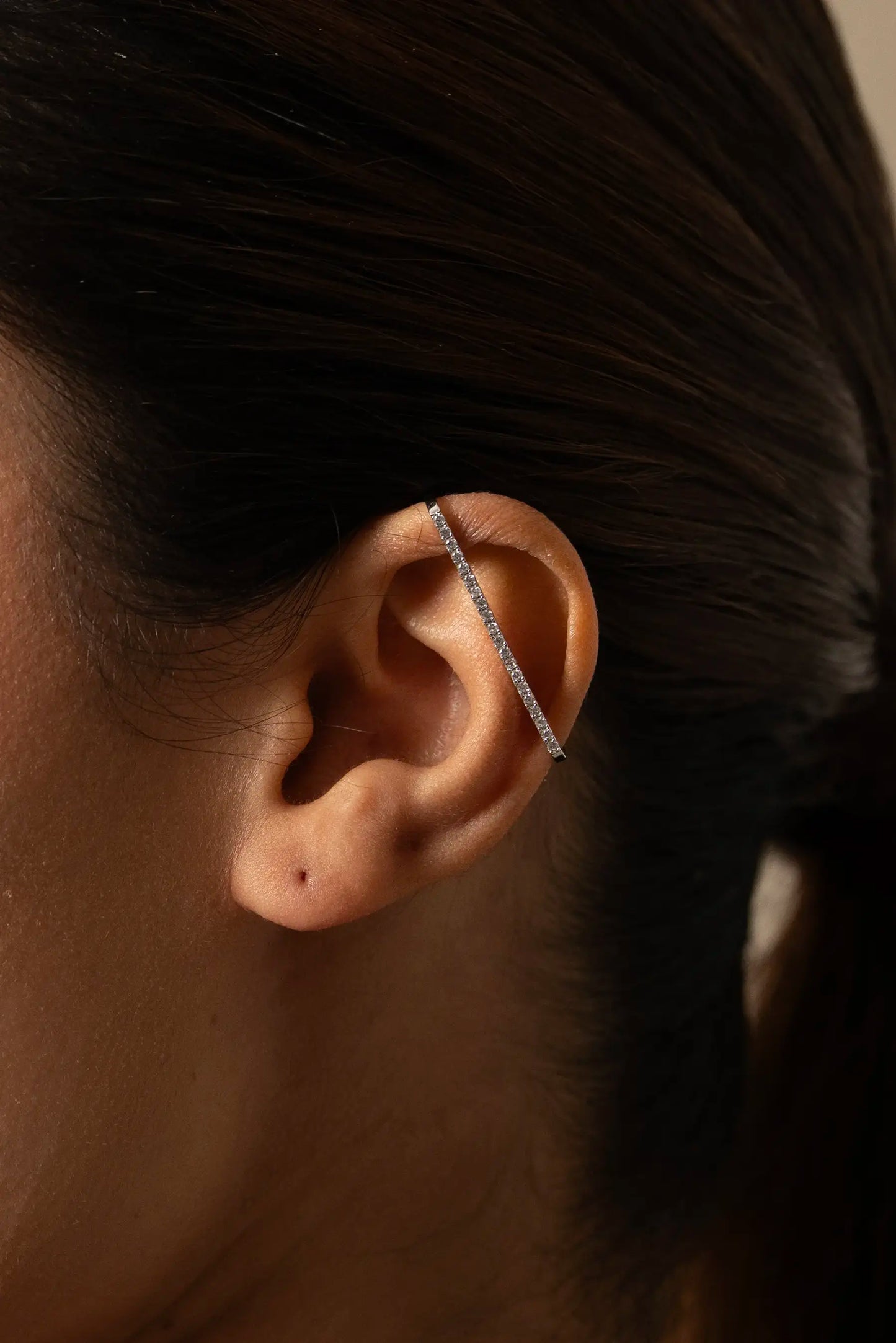 Detailed view of a silver ear cuff with sparkling stones worn along the ear, stylish contemporary jewelry