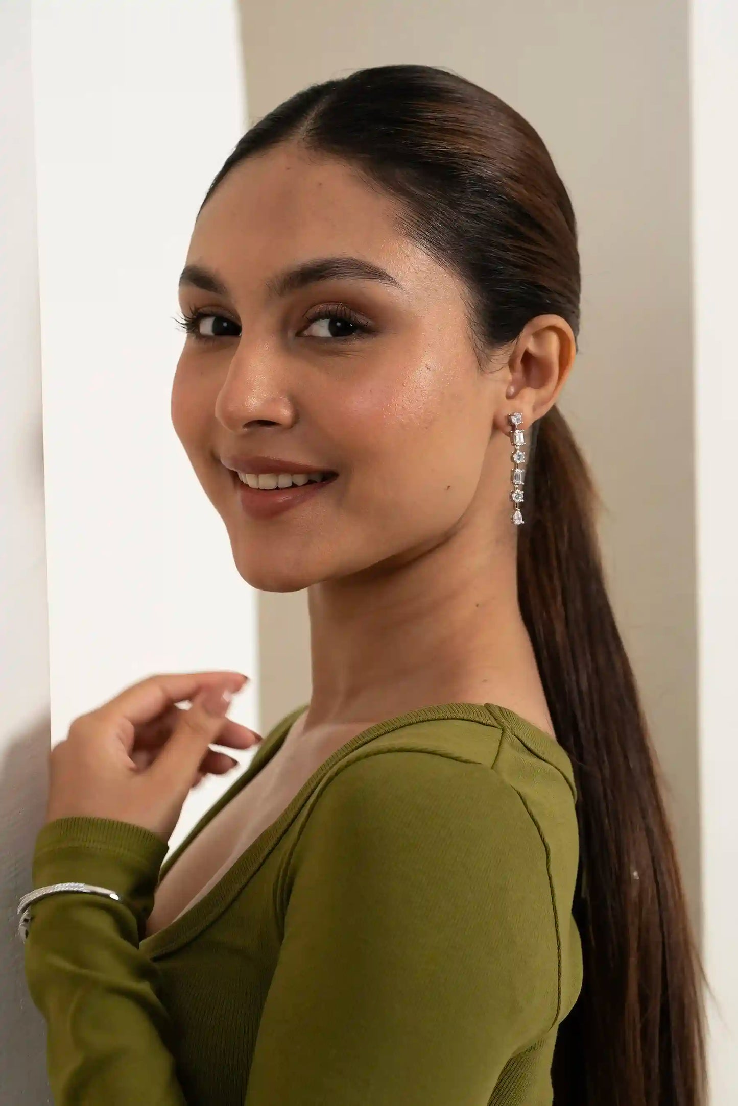 Smiling woman wearing long dangling diamond earrings, captured in a stylish indoor portrait setting
