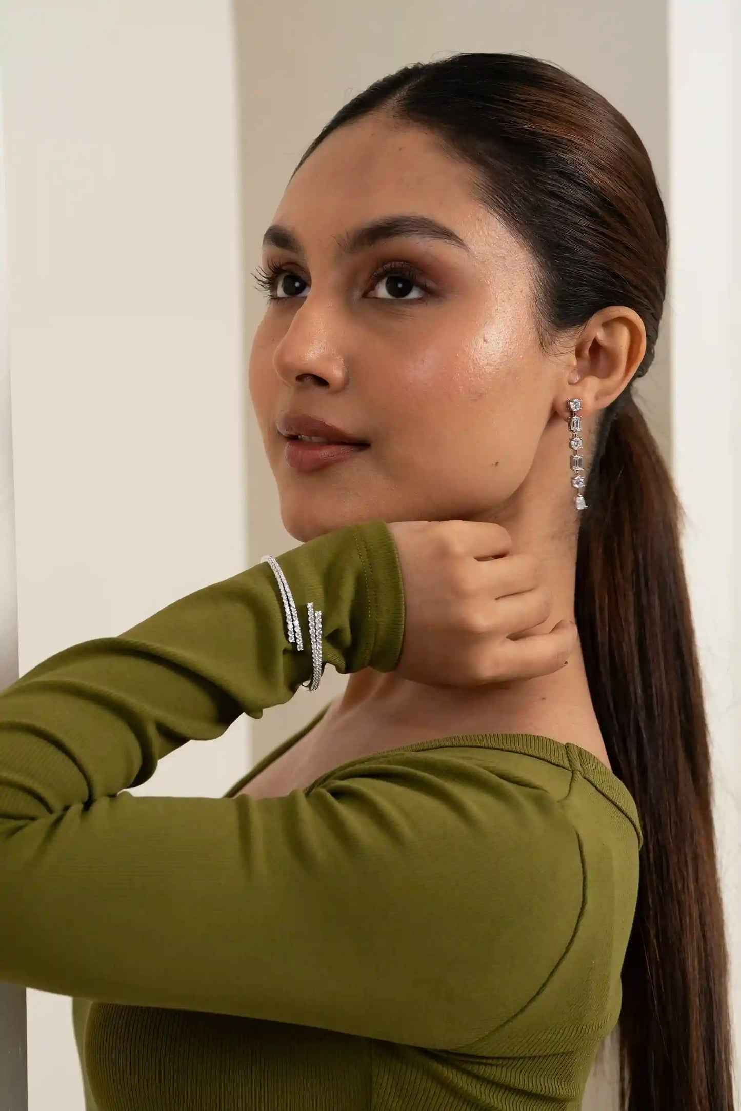 Fashion model posing in green dress with crystal drop earrings and layered bracelets, contemporary jewelry styling