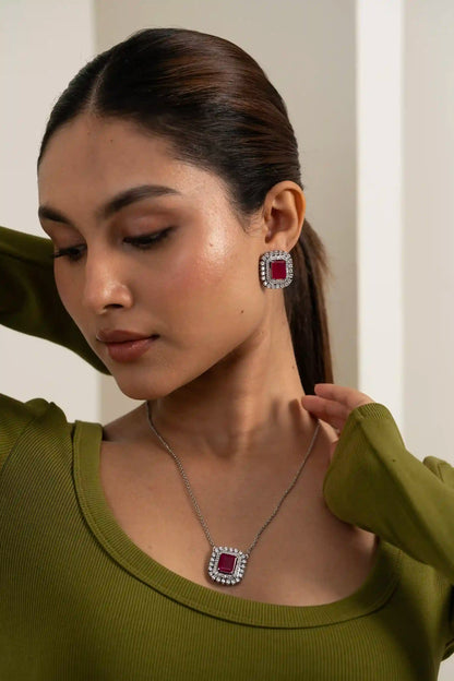 Elegant ruby cushion halo jewellery set featuring diamond-framed pendant and earrings on modern model