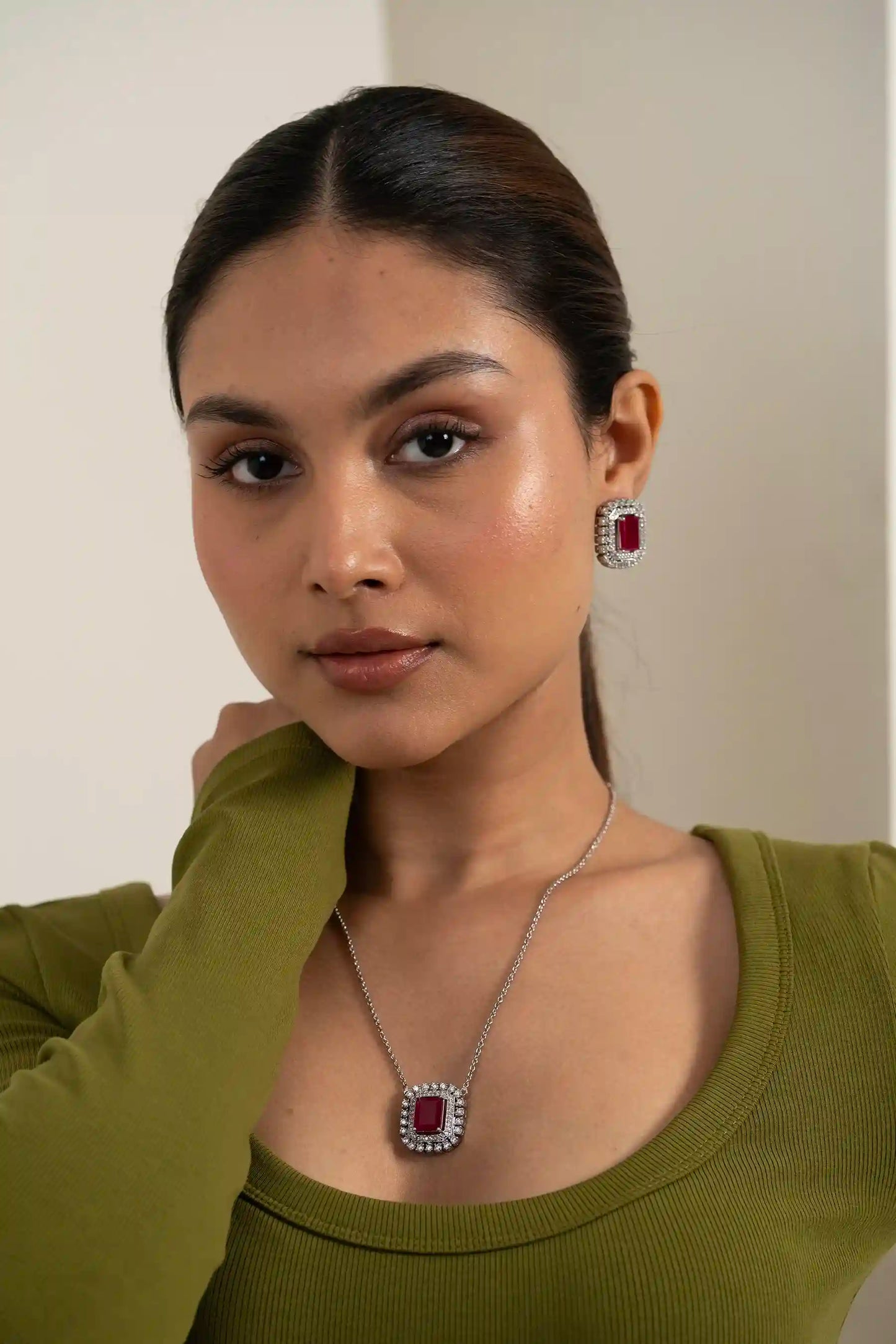 Model wearing ruby cushion halo necklace and matching diamond earrings with elegant side profile pose