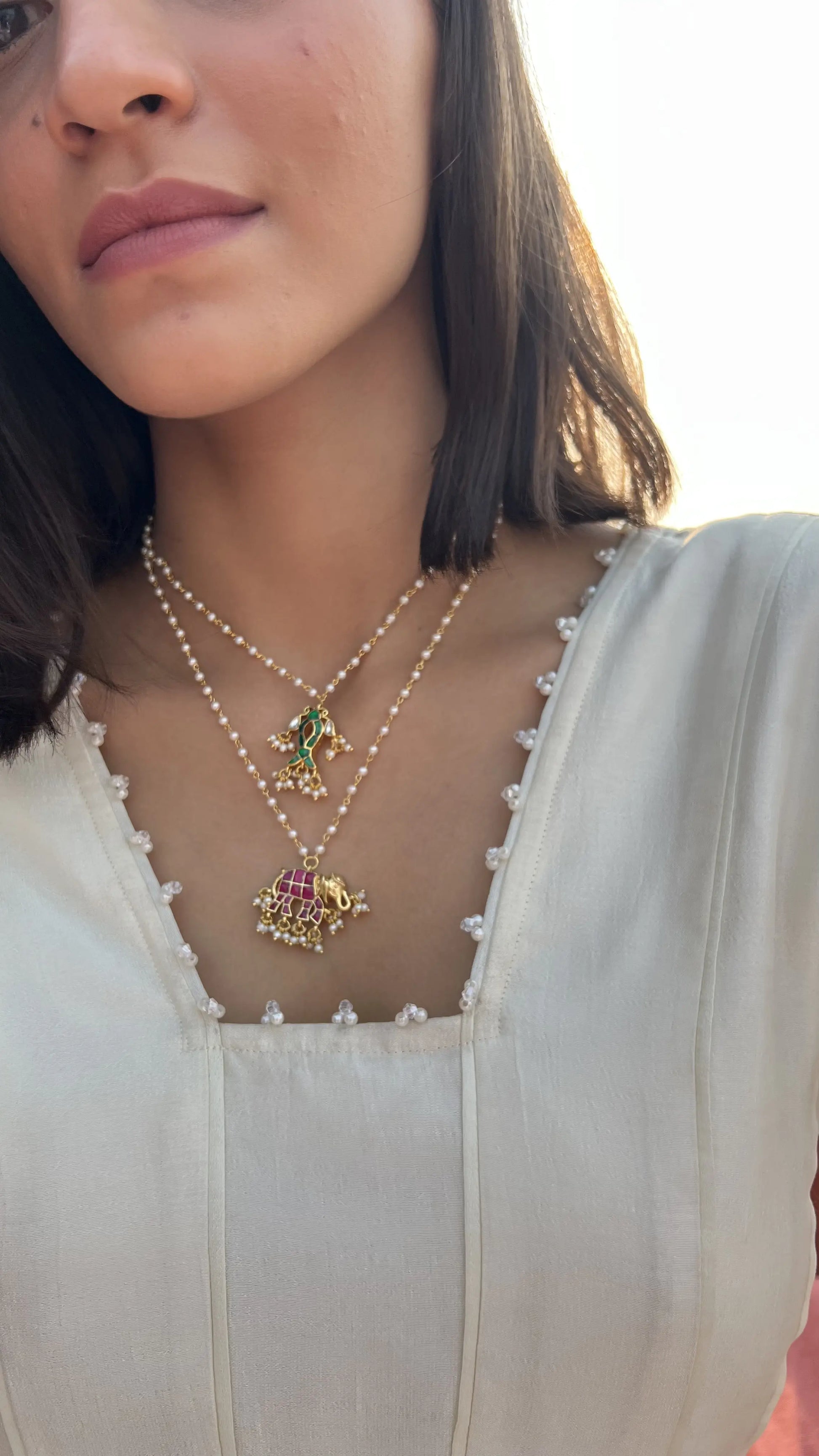 Fine jewelry composition highlighting dual strands of pearl and gold chains with decorative enamel charms in a traditional style.
