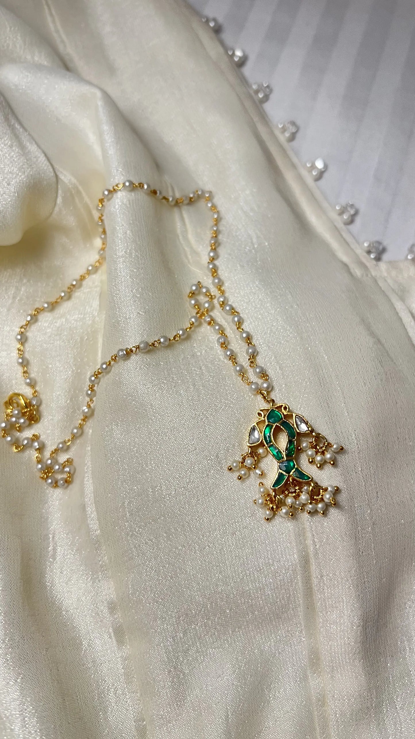 Sophisticated neckline detail featuring layered pearl necklaces with intricate gold pendants accented by colorful enamel work.
