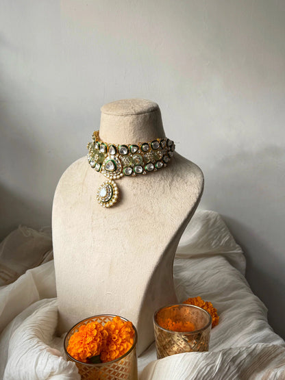 Bridal gold choker necklace with kundan stones and green detailing on neutral display stand
