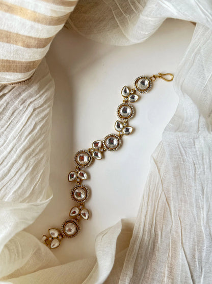 Elegant gold bracelet with kundan stones and teardrop crystals on soft fabric background
