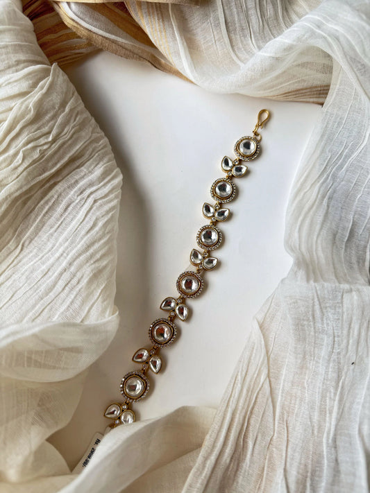 Traditional gold bracelet with clear kundan stones and intricate design in soft lighting
