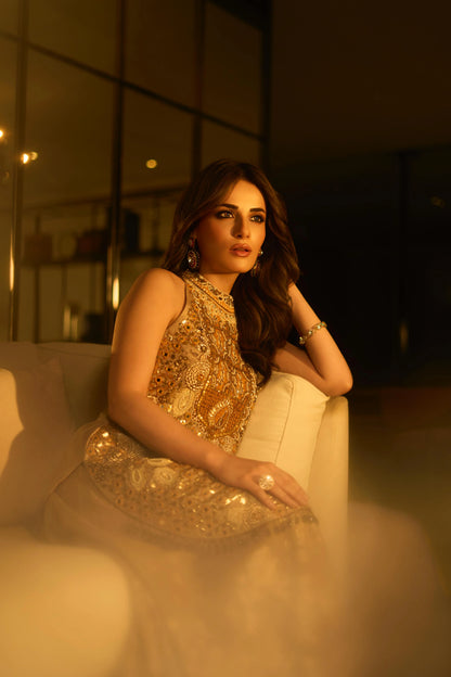 Elegant portrait of a woman wearing a heavily embellished gold dress and jewelry in a luxurious indoor setting
