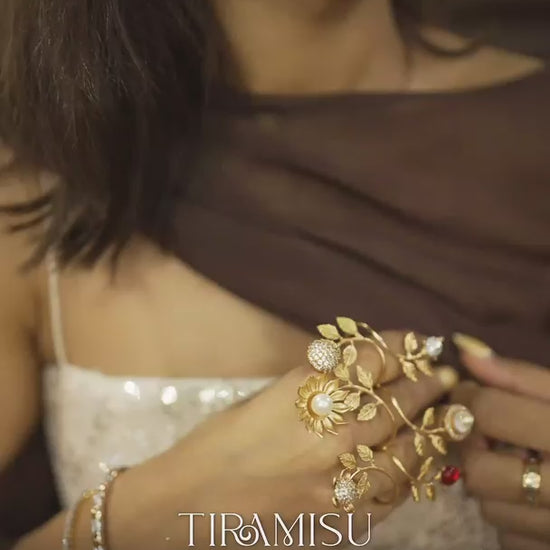 Close-up of woman wearing intricate gold hand jewelry with leaf design and gemstone rings
