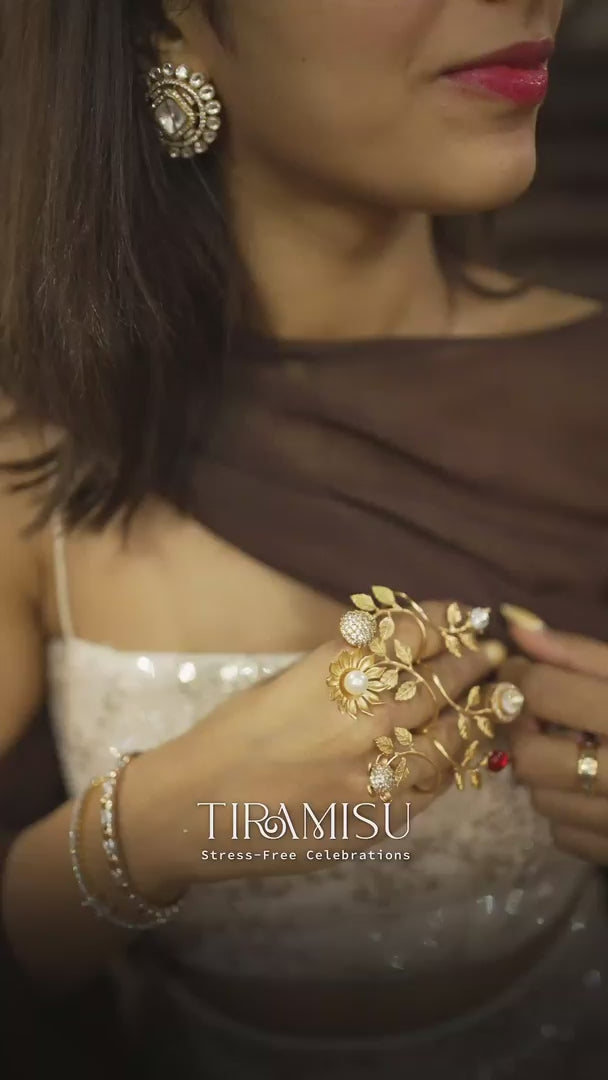 Close-up of woman wearing intricate gold hand jewelry with leaf design and gemstone rings
