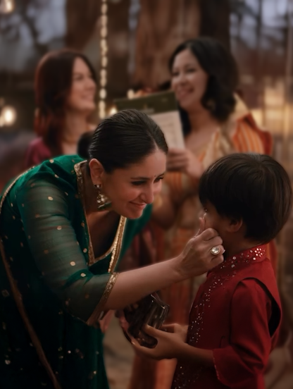 Festive scene with woman in green saree engaging lovingly with child at celebration
